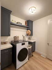 Laundry area with washer / dryer, light wood-type flooring, a textured ceiling, and cabinet space