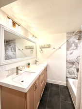 Full bath featuring double vanity, a textured ceiling, a combined bath / shower with marble appearance, and dark tile patterned floors