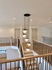 Hallway featuring light wood-type flooring, a textured ceiling, an upstairs landing, and recessed lighting