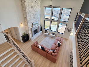 Living area with a high ceiling, a stone fireplace, light wood-type flooring, and ceiling fan