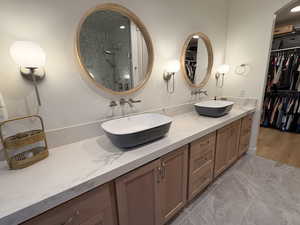 Full bath with double vanity, a stall shower, light marble finish floors, and a spacious closet