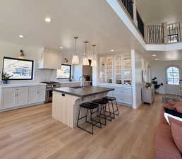 Dual tone kitchen featuring a kitchen breakfast bar, stainless steel range, a kitchen island with sink, hanging light fixtures, and light wood finished floors