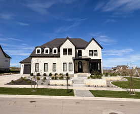French country-inspired facade with stacked stone siding, a shingled roof, concrete driveway, an attached garage, side parking, and a front lawn