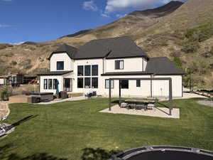 Back of house with an outdoor fire pit, a hot tub, a mountain view, roof with shingles, and a patio
