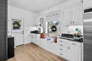 Kitchen with white cabinets, stainless steel refrigerator, healthy amount of natural light, crown molding, and light wood-style floors