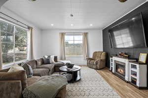 Living room with light wood-type flooring, a glass covered fireplace, recessed lighting, and wood walls