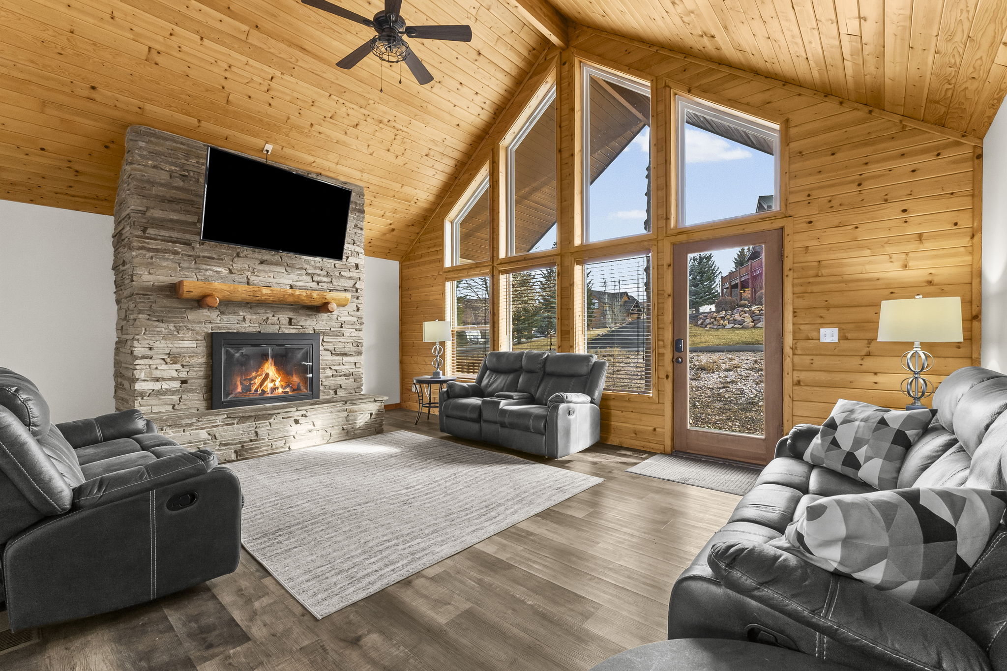 Living room with a high wooden ceiling, wood finished floors, a ceiling fan, and a stone fireplace