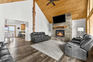 Living room with plenty of natural light, a vaulted wood ceiling, a stone fireplace, dark wood-style flooring, and a ceiling fan