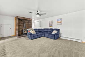 Living room with a baseboard radiator, a wood stove, a ceiling fan, and carpet