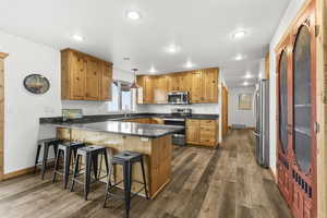 Kitchen with a peninsula, dark stone countertops, decorative light fixtures, stainless steel appliances, and dark wood-style floors
