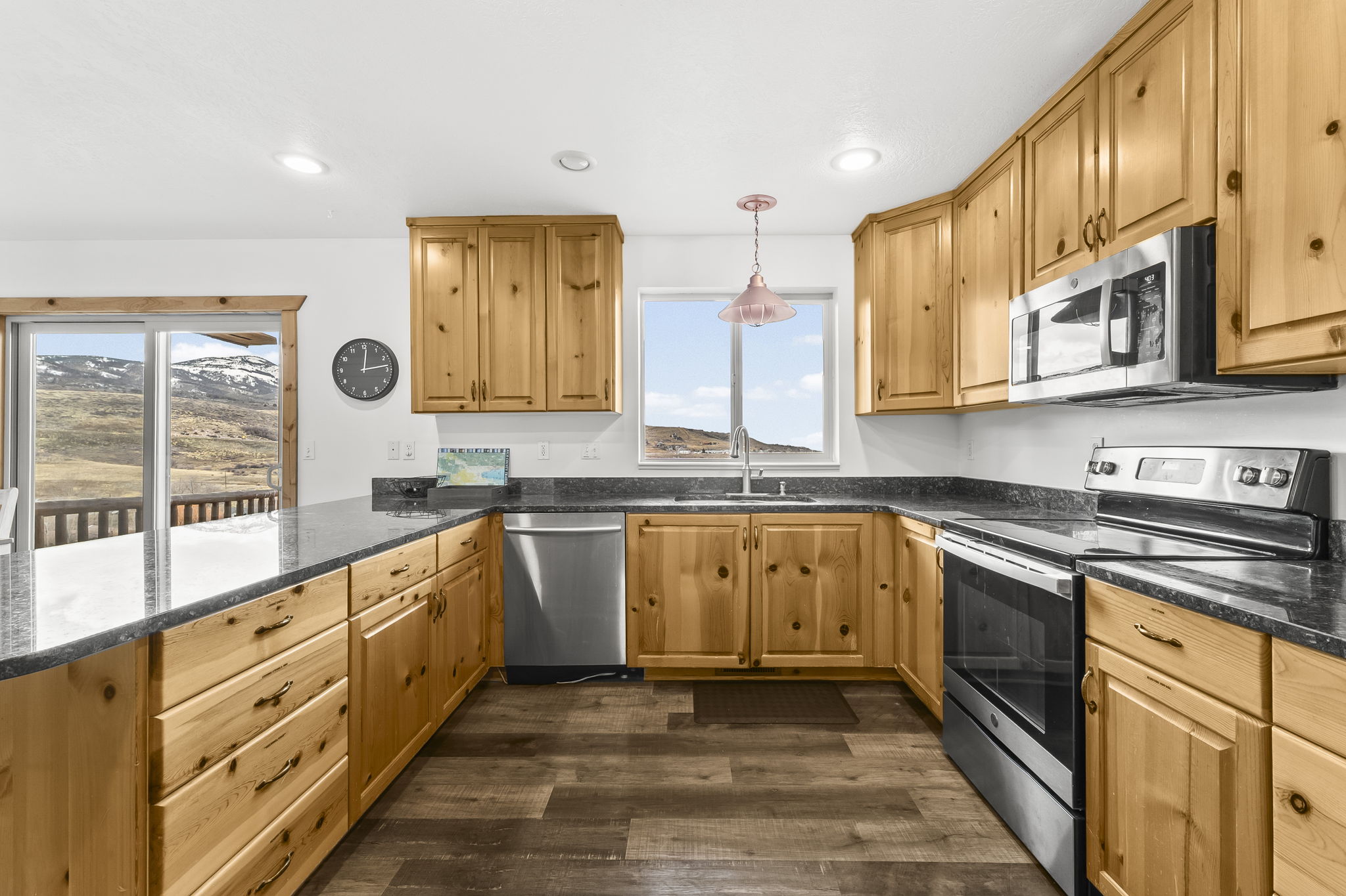Kitchen featuring stainless steel appliances, dark stone counters, decorative light fixtures, dark wood-style floors, and a peninsula