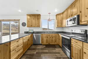 Kitchen featuring stainless steel appliances, dark stone counters, decorative light fixtures, dark wood-style floors, and a peninsula