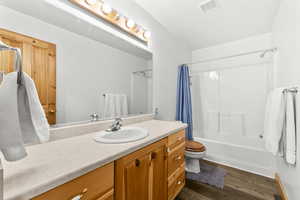 Full bath featuring vanity, shower / bath combination with curtain, and dark wood-type flooring