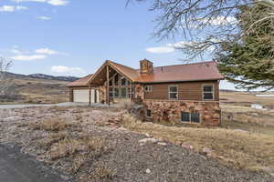 View of front of property featuring stone siding, a chimney, a metal roof, faux log siding, and a patio