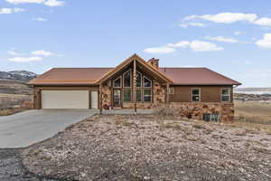 Log-style house with stone siding, a chimney, a metal roof, concrete driveway, and a garage