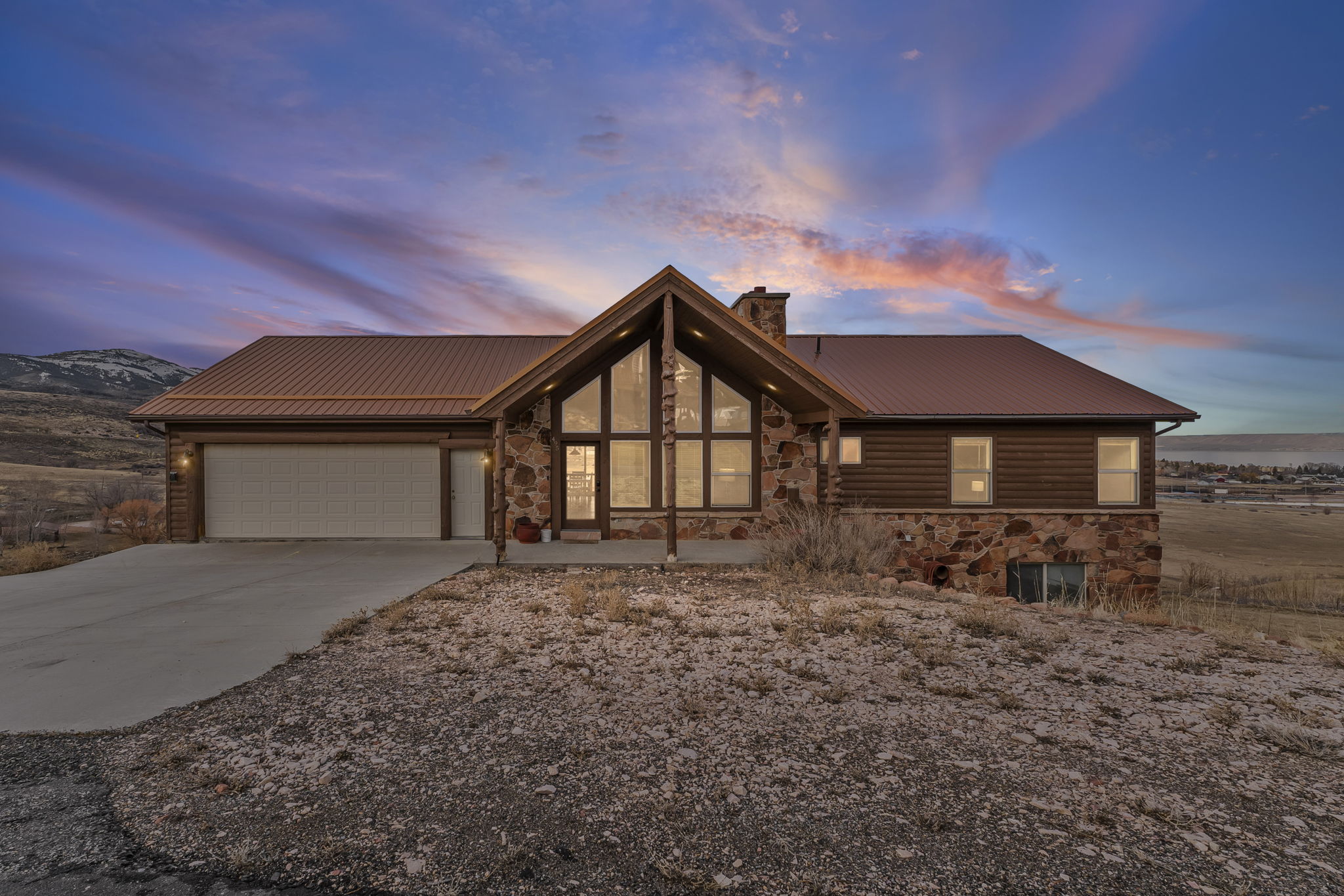 View of front of property with stone siding, a chimney, a metal roof, and driveway