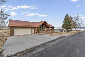 Cabin with stone siding, concrete driveway, a metal roof, a garage, and a porch