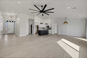 Unfurnished living room featuring a chandelier, light wood-style flooring, and a ceiling fan