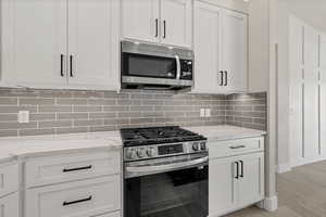 Kitchen featuring stainless steel appliances, white cabinetry, and light stone counters