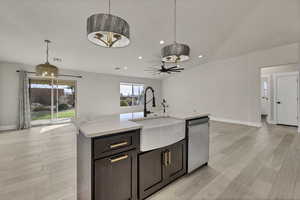 Kitchen with open floor plan, vaulted ceiling, light wood-type flooring, a kitchen island with sink, and ceiling fan