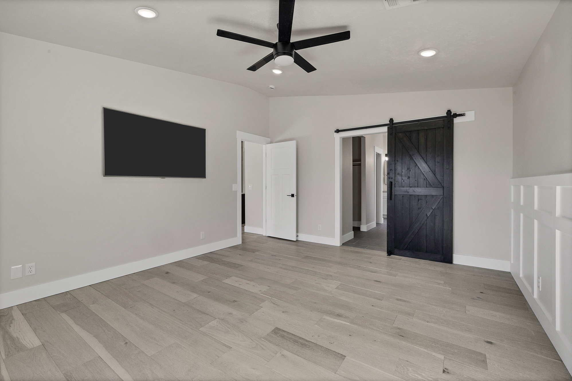 Unfurnished bedroom with a barn door, ceiling fan, light wood-style floors, recessed lighting, and vaulted ceiling