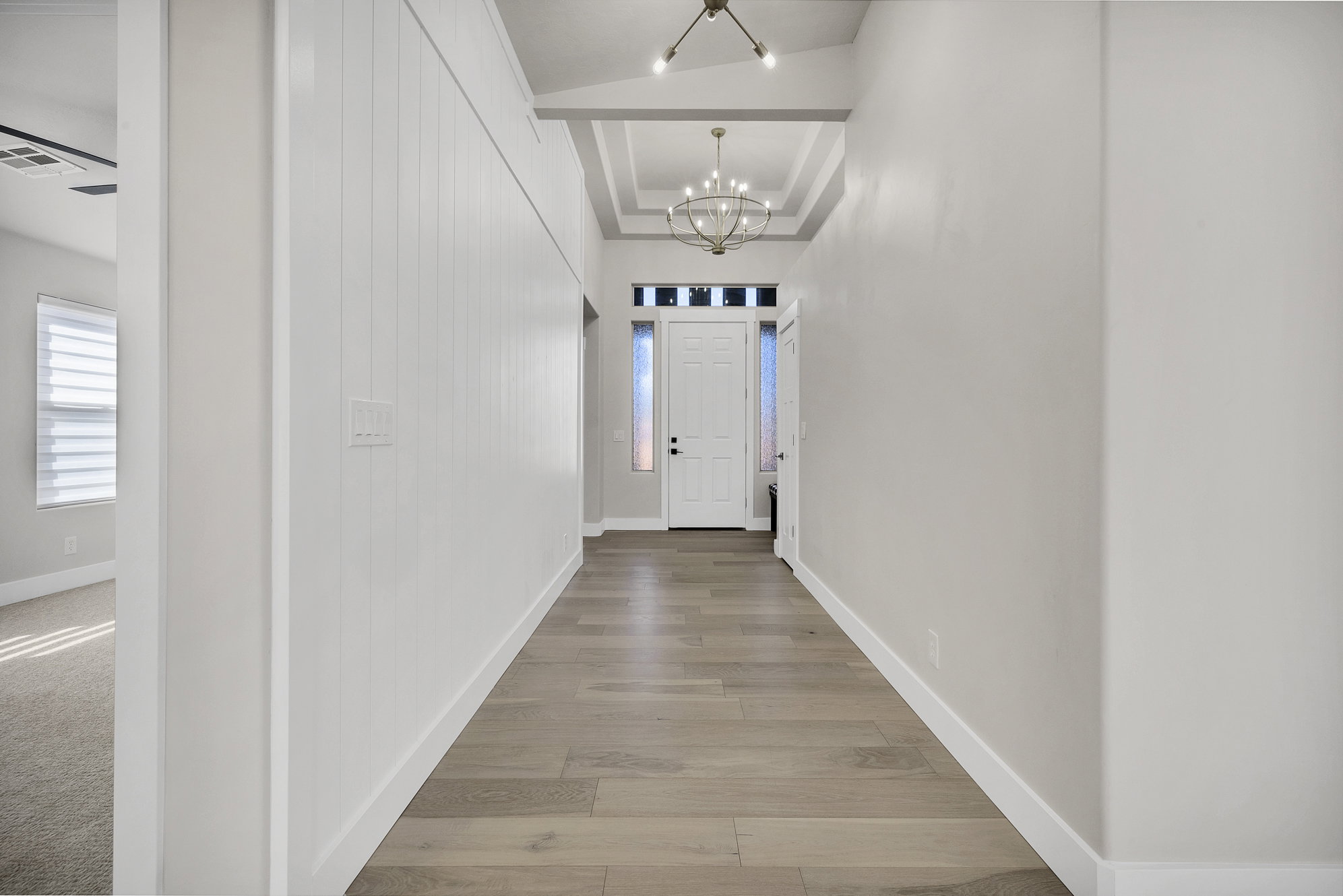 Corridor featuring a raised ceiling, a chandelier, and light wood-type flooring