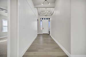 Corridor featuring a raised ceiling, a chandelier, and light wood-type flooring