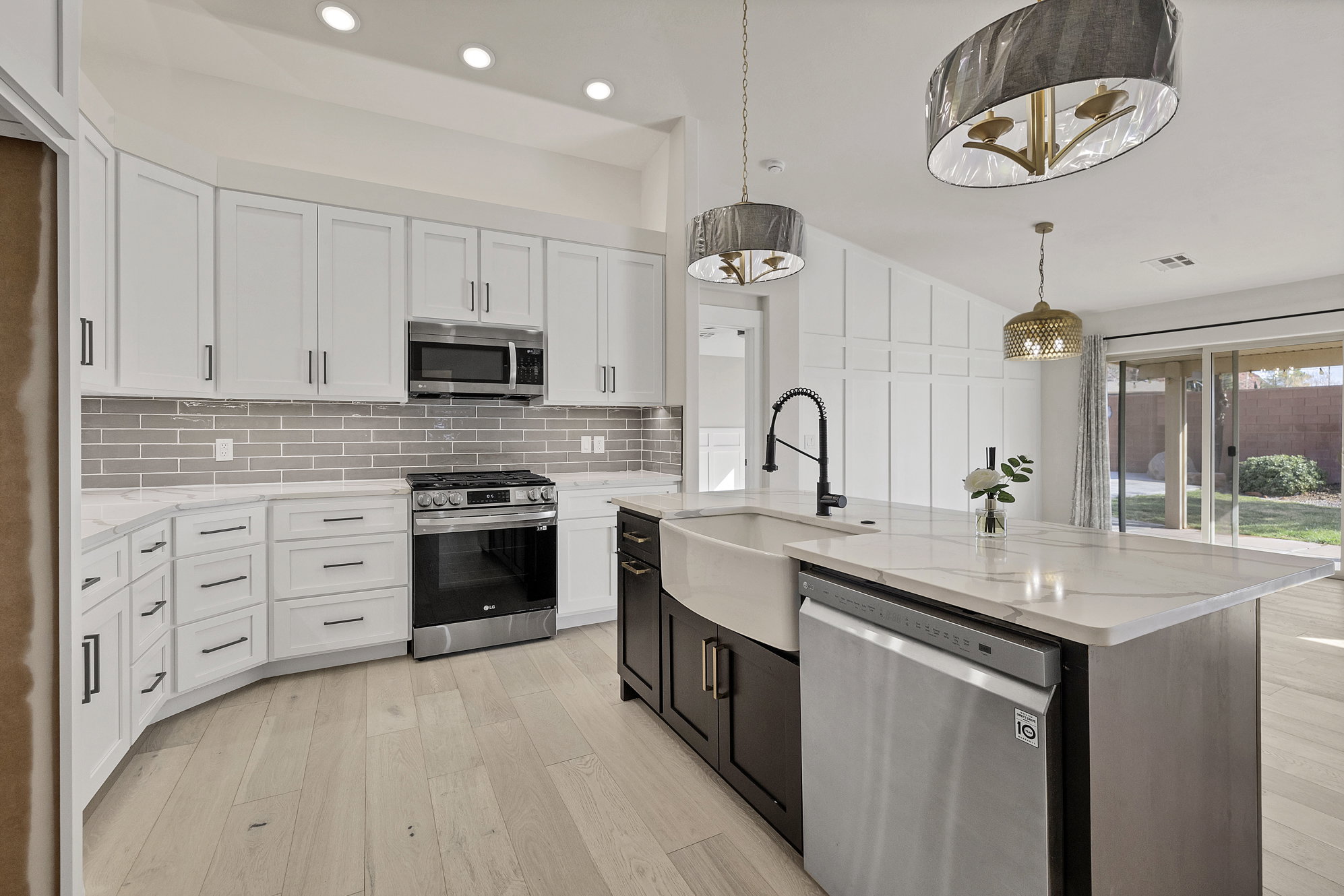 Kitchen featuring two tone cabinetry, stainless steel appliances, light wood-style floors, light stone countertops, and tasteful backsplash