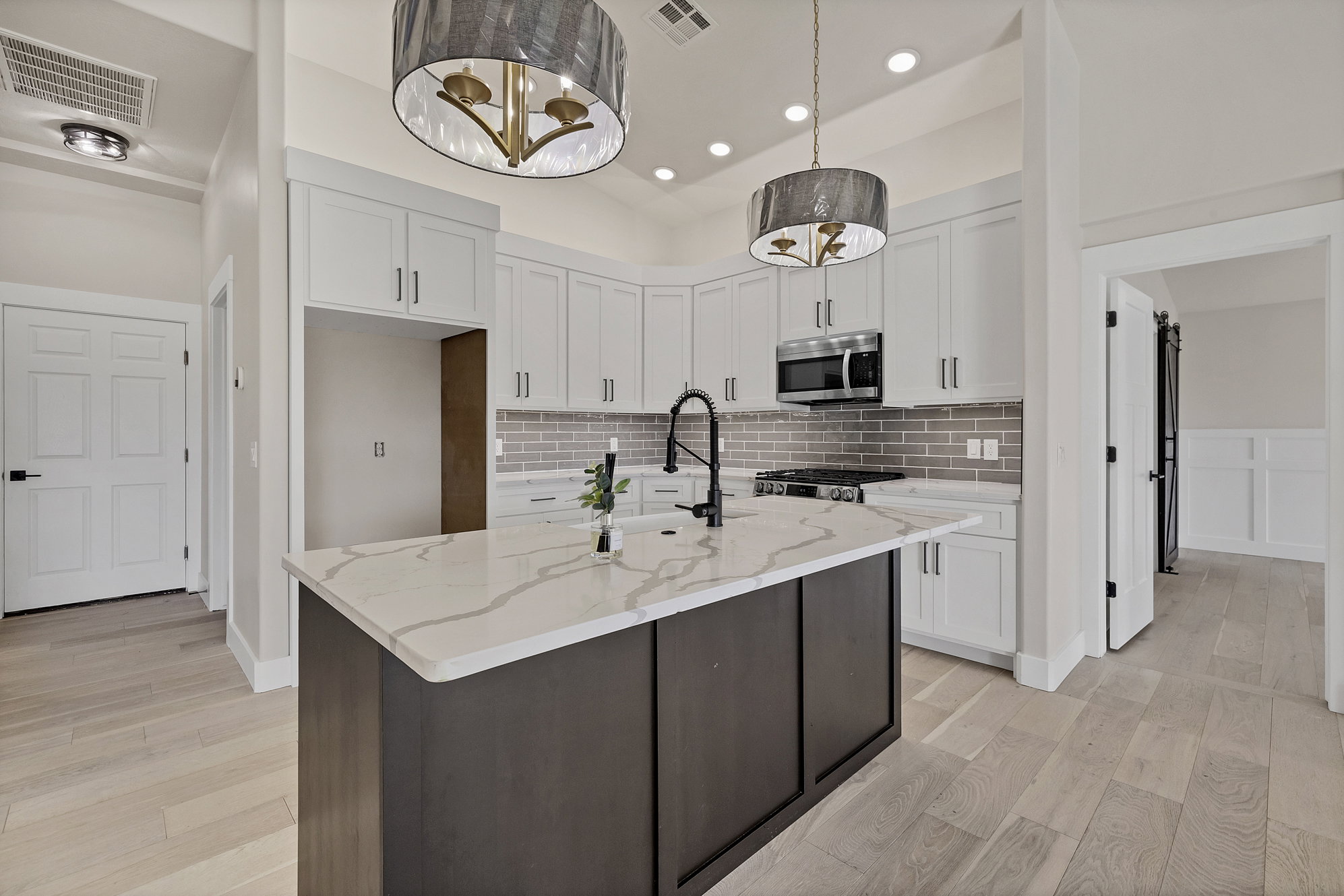 Kitchen featuring dual tone cabinetry, light stone countertops, an island with sink, light wood-type flooring, and stainless steel appliances