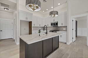 Kitchen featuring dual tone cabinetry, light stone countertops, an island with sink, light wood-type flooring, and stainless steel appliances