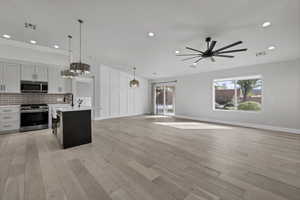 Two tone kitchen with stainless steel appliances, open floor plan, dual tone cabinets, decorative light fixtures, and an island with sink