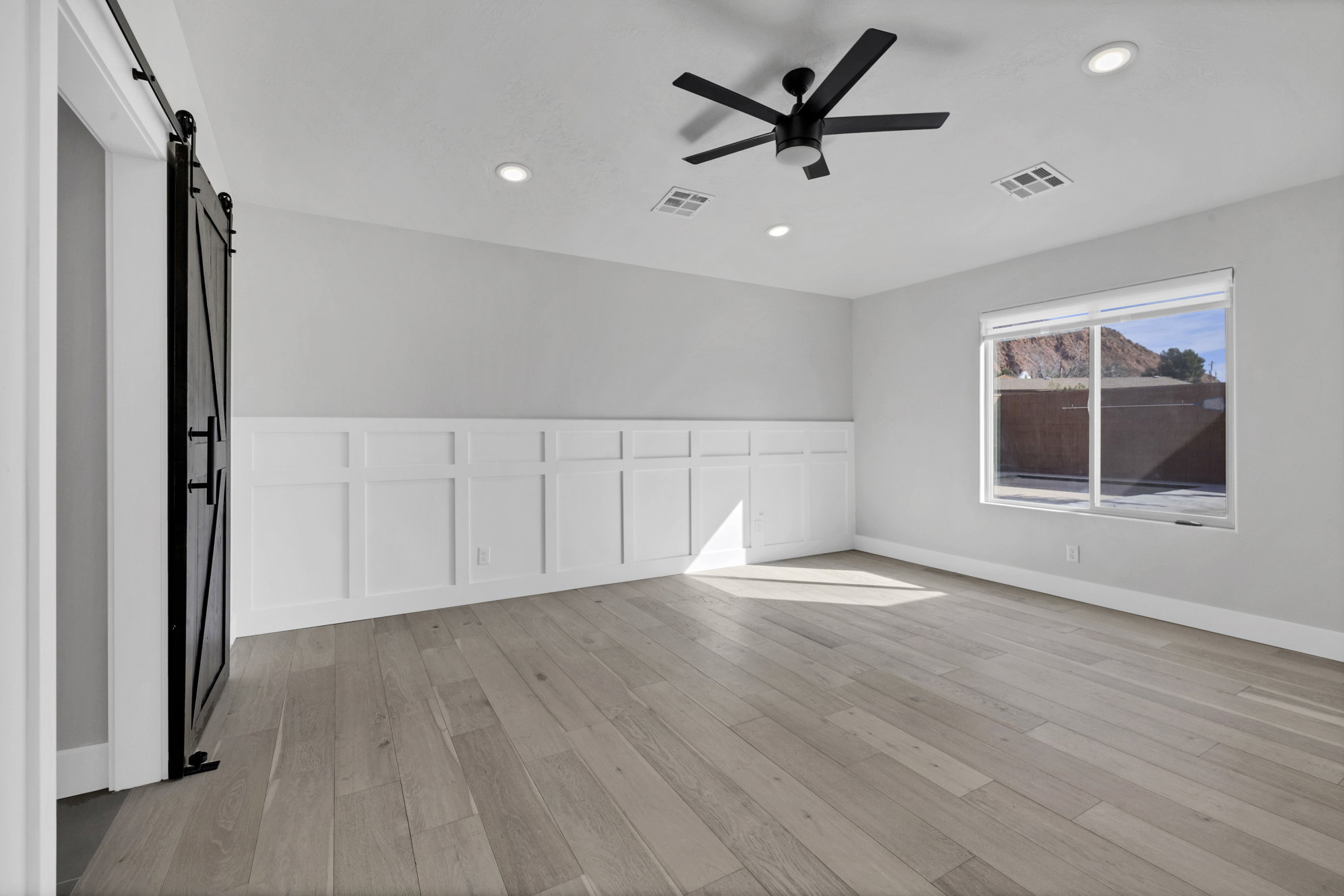 Spare room featuring a barn door, light wood finished floors, a decorative wall, ceiling fan, and wainscoting