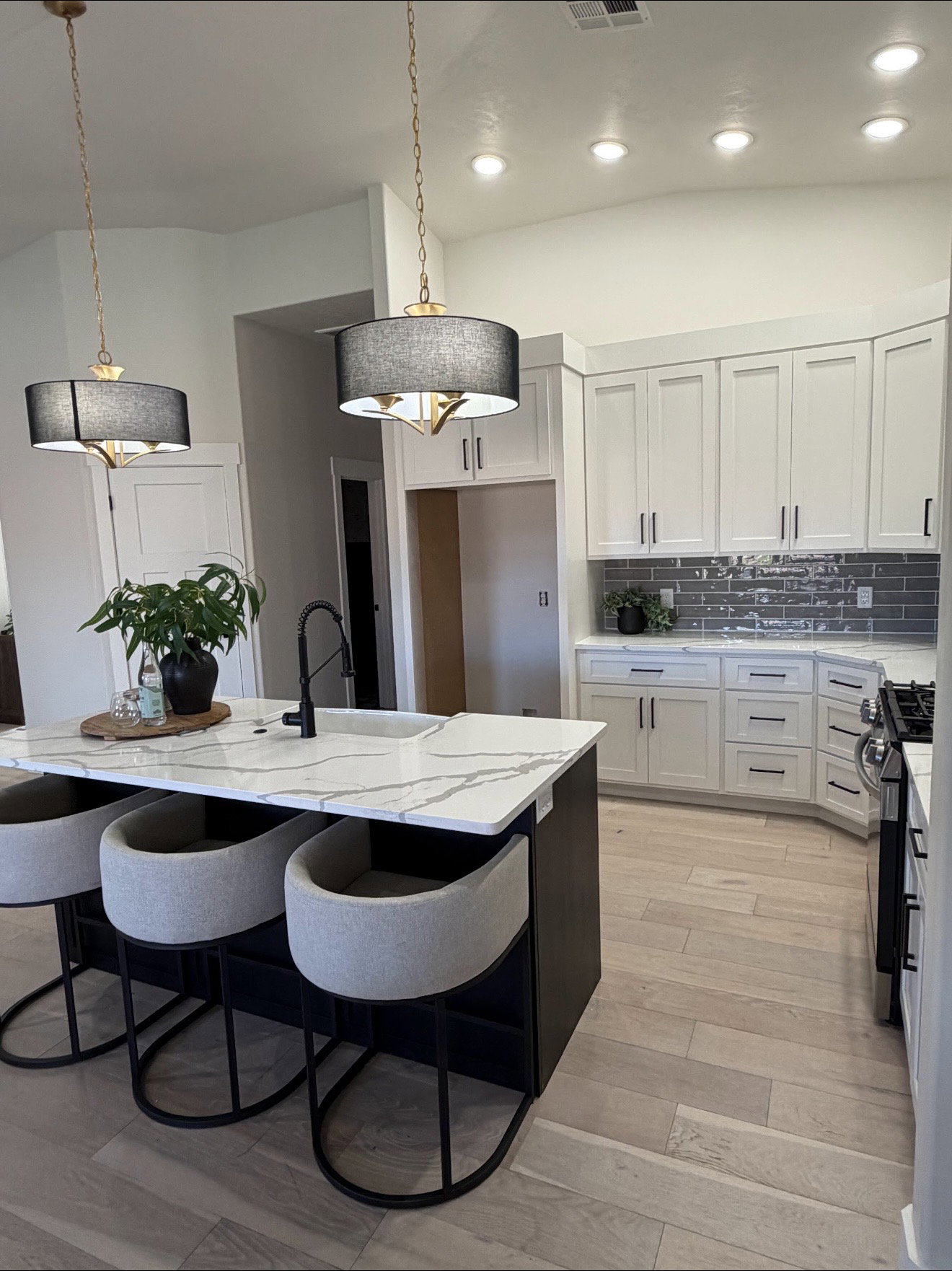 Spacious kitchen featuring a large island with a waterfall-edge countertop, white shaker-style cabinetry, a gray subway tile backsplash, and light wood-finish flooring