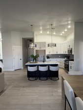Gourmet kitchen featuring a central island with countertop seating, light wood-finish flooring, white cabinetry, a subway tile backsplash, and recessed lighting