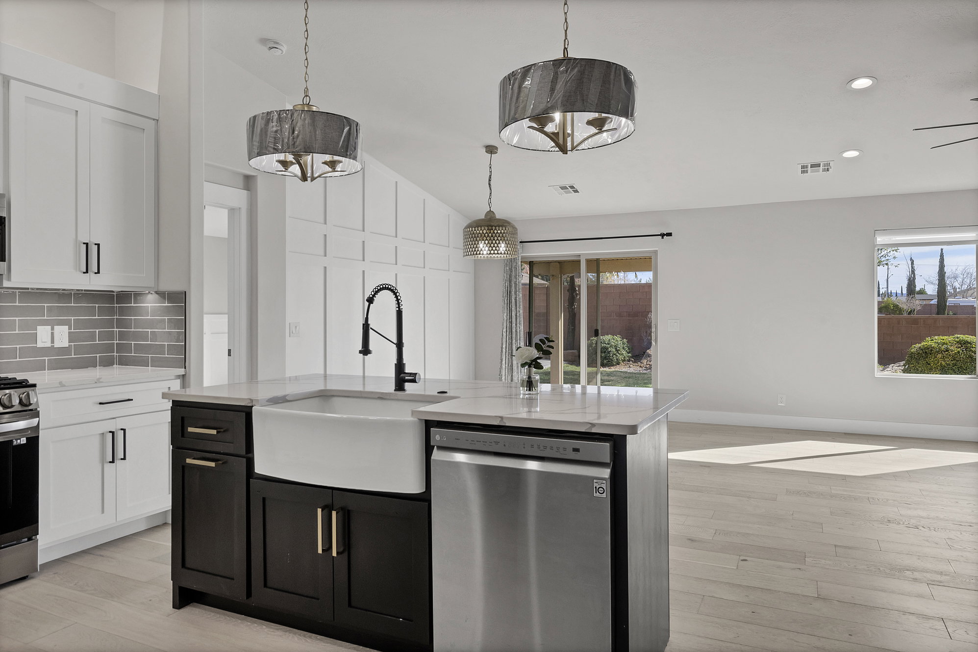 Kitchen with two tone cabinetry, stainless steel appliances, light wood-style flooring, vaulted ceiling, and an island with sink