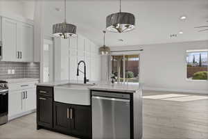 Kitchen with two tone cabinetry, stainless steel appliances, light wood-style flooring, vaulted ceiling, and an island with sink