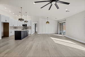 Kitchen with vaulted ceiling, open floor plan, a center island with sink, light stone counters, and a ceiling fan