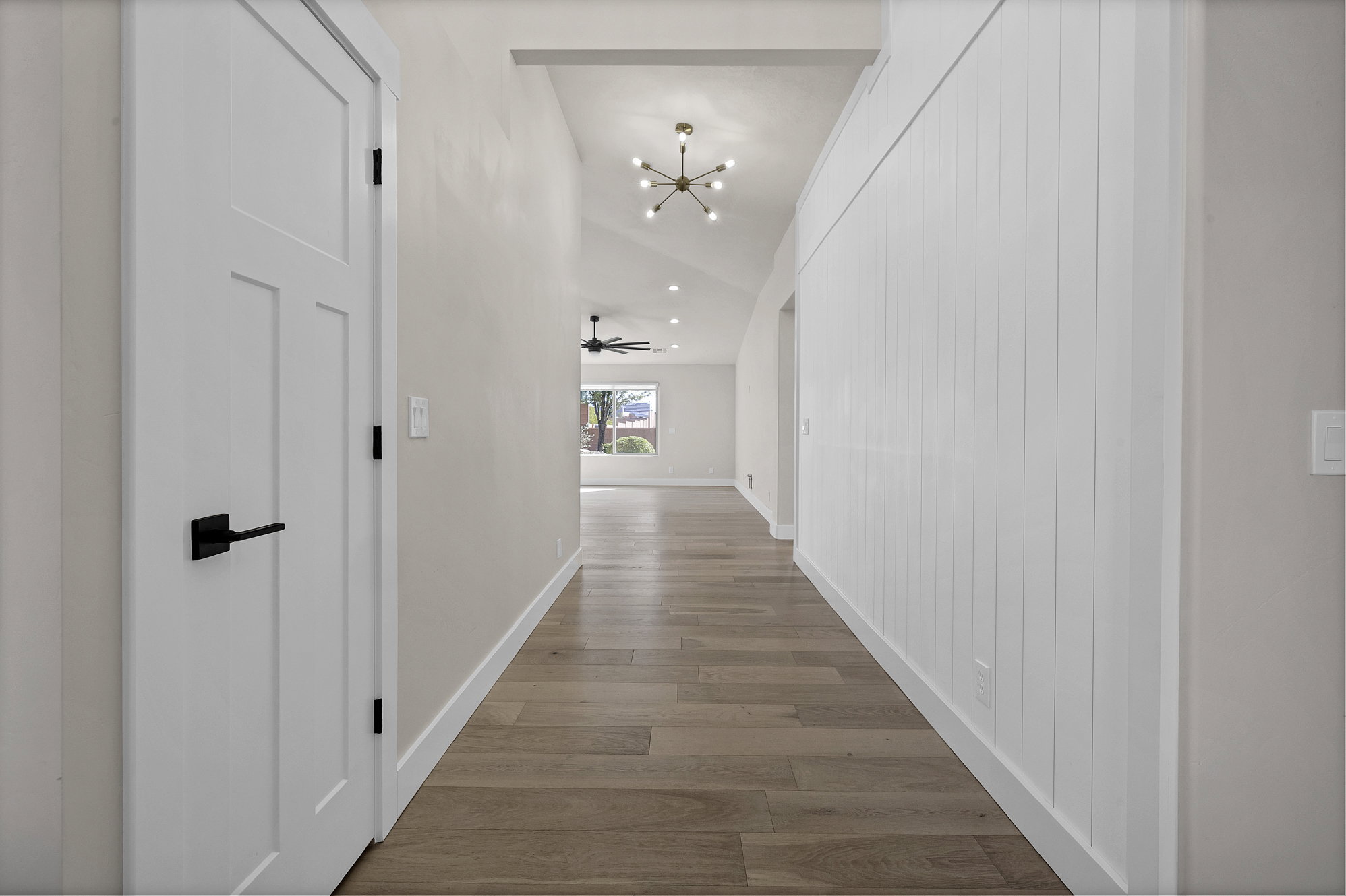 Corridor with vaulted ceiling, light wood-type flooring, and a chandelier