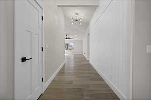 Corridor with vaulted ceiling, light wood-type flooring, and a chandelier