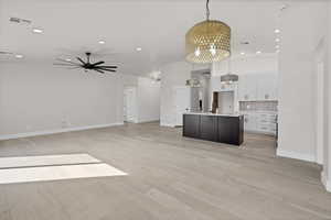 Kitchen with two tone cabinets, an island with sink, open floor plan, a ceiling fan, and light wood-style floors