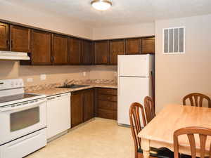 Kitchen featuring white appliances, dark wood finish cabinets, light countertops, light floors, and a textured ceiling