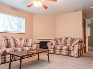 Carpeted living area featuring ceiling fan and a fireplace