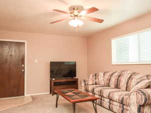 Carpeted living area featuring ceiling fan and baseboards
