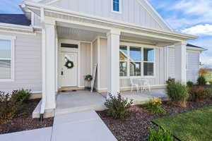 Doorway to property with covered porch, board and batten siding, and roof with shingles