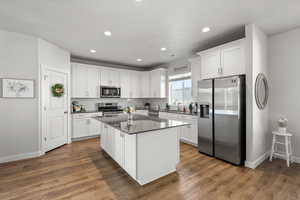 Kitchen featuring stainless steel appliances, white cabinets, a center island, dark wood-type flooring, and recessed lighting