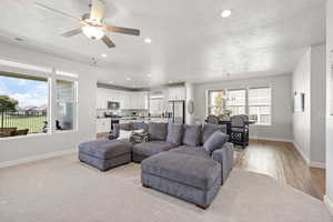 Living room featuring a ceiling fan, a textured ceiling, suspended lighting, and light carpet