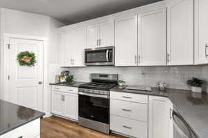 Kitchen with stainless steel appliances, white cabinetry, wood-style floors, dark stone counters, and tasteful backsplash