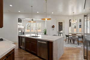 Kitchen featuring dark wood-style floors, stainless steel appliances, a kitchen island with sink, and light stone countertops