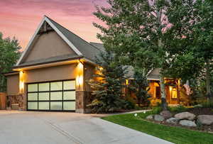 View of front of property featuring roof with shingles, stucco siding, stone siding, driveway, and an attached garage