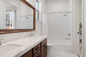 Full bath with double vanity, shower / bath combo with shower curtain, and light tile patterned floors